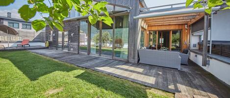 Een modern huis met een terras, een patio met buitenmeubilair en uitzicht op een meer.