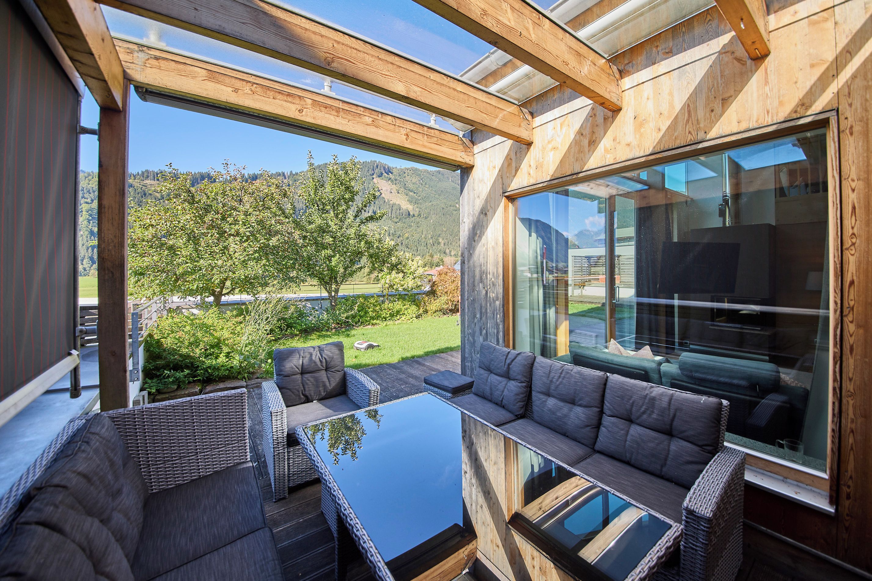 Een modern buitenverblijf met rieten meubilair en glazen tafels, met uitzicht op een schilderachtig landschap met bomen en heuvels.