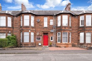A two-story brick house with a red door, multiple windows, and satellite dishes. - Cosy Kilmarnock Apartment (East Ayrshire Council)