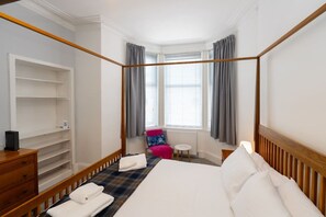 A hotel room with a four-poster bed, a wooden dresser, a chair, and a small table. - Cosy Kilmarnock Apartment (East Ayrshire Council)