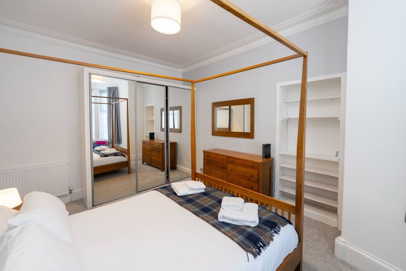 A four-poster bed with a mirror above it, a wooden dresser, and a walk-in closet with shelves.