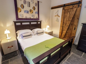 Ein Schlafzimmer mit Bett, Nachttischen, einer Lampe, einem hölzernen Kopfteil, einer grünen Tagesdecke, einer hölzernen Bank und einem an der Wand befestigten Kunstwerk.