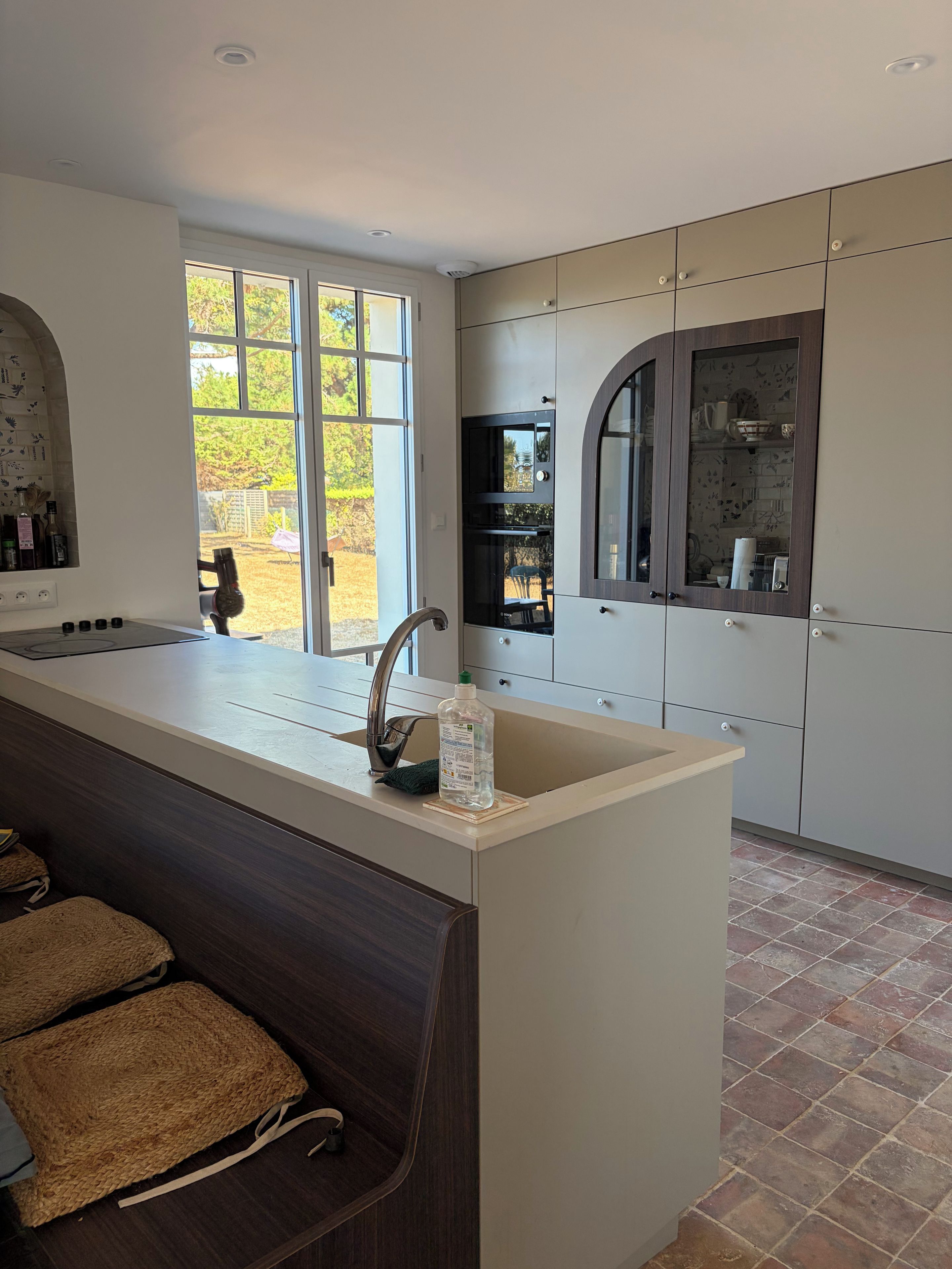 A modern kitchen with a central island, a built-in oven, and a large window.