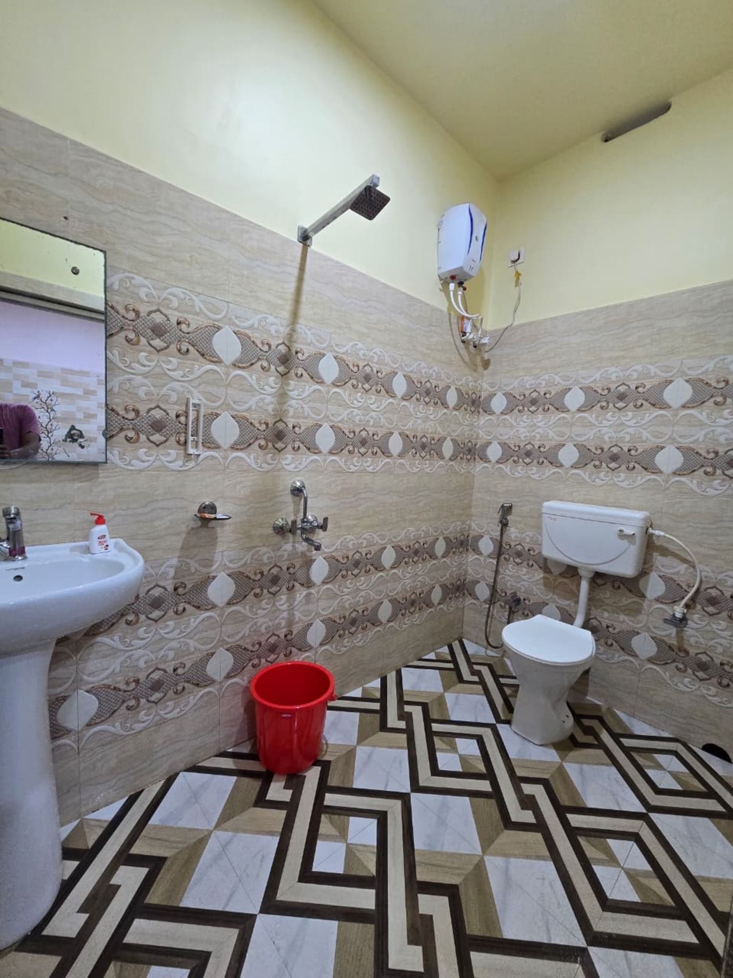 Une salle de bain avec un lavabo, des toilettes, une douche et un seau rouge posé sur le sol.