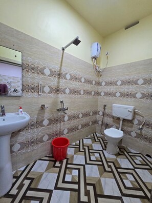 Une salle de bain avec un lavabo, des toilettes, une douche et un seau rouge posé sur le sol.