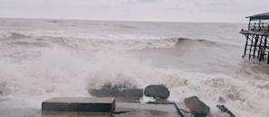 A pier extending into a rough sea with waves crashing over the edge. - SINGHBHUM-The Shore (Kanthi)