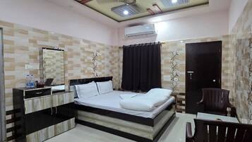 Une chambre d’hôtel équipée d’un lit, d’un bureau, d’une chaise, d’une armoire et d’un ventilateur de plafond.
