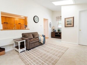 A living room with a sofa, a small table, a clock, and a door leading to another room. - Oneida Lake House | Fire Pit | Dock | Sleeps 9 (Bernhards Bay)