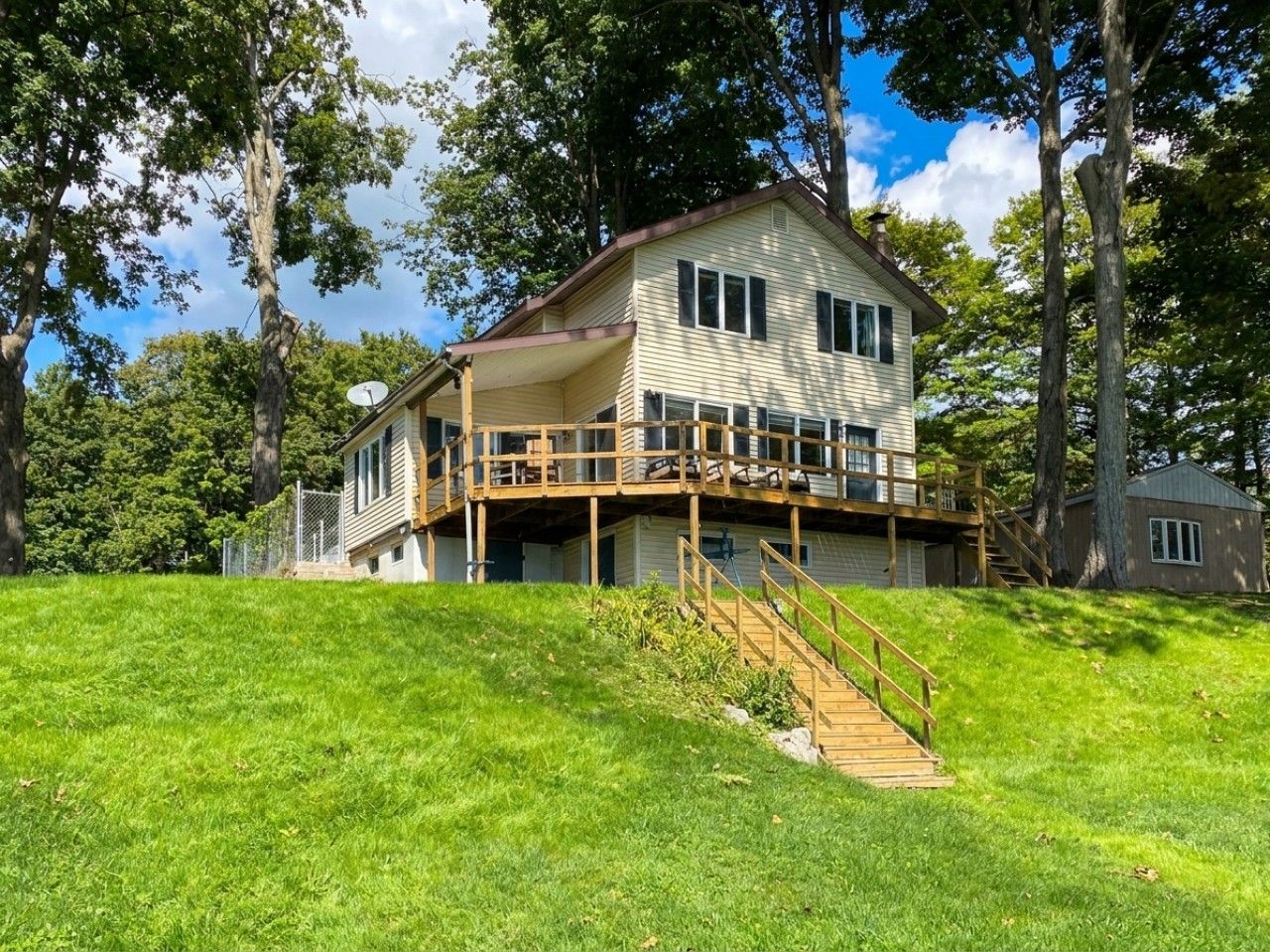 Une maison à deux étages dotée d’une terrasse en bois et d’un escalier menant à un balcon situé au deuxième étage.