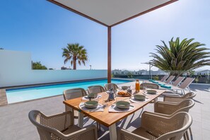 A poolside dining area with a table set for two, overlooking a swimming pool. - Vacation Villa 'Ereza Royal Family Hoopoe 119' with Private Pool, Wi-Fi and Air Conditioning (Playa Blanca)