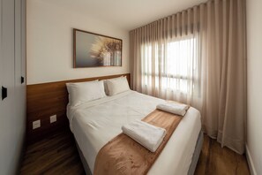 A hotel room with a large bed, a wooden headboard, a painting on the wall, and sheer curtains. - Agami by Bhomy  (São Paulo)
