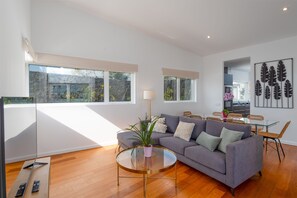 Uma sala de estar moderna com um sofá cinza, uma mesa de centro de vidro e um espaço de jantar com cadeiras de vime.