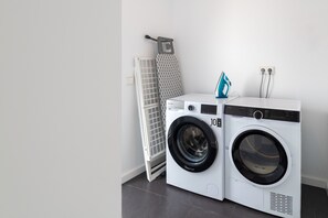 Uma lavanderia moderna com máquina de lavar frontal, secadora, varal e centro de passar roupa fixado na parede.