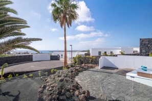 A rooftop terrace with a palm tree, rocky terrain, and a view of the sea. - Vacation Villa 'Ereza Royal Family Hoopoe 117' with Private Pool, Wi-Fi and Air Conditioning (Playa Blanca)