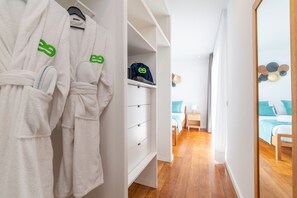 Quarto de hotel com guarda-roupa, cama com roupa de cama azul e chão de madeira.