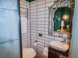 A bathroom with a white tiled wall, a wooden vanity with a sink, a mirror with a decorative frame, and a towel rack. - The Carriages (Barry)