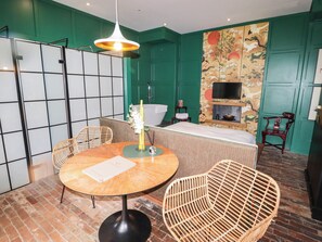 A room with a round table, wicker chairs, a bed, a TV, and a green wall with traditional artwork. - The Carriages (Barry)