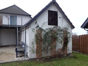 Ein kleines Haus mit geneigtem Dach, einem Holzzaun und einem Gartenbereich mit einer Bank.