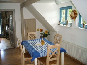 Ein Essbereich mit kariertem Tischläufer, Holzkästen, einer Vase mit Blumen und einem Fenster mit einem Kranz.