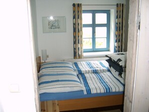 Ein Schlafzimmer mit einem Bett, einem Fenster mit Vorhängen, einem Heizkörper und einer Wandleuchte.