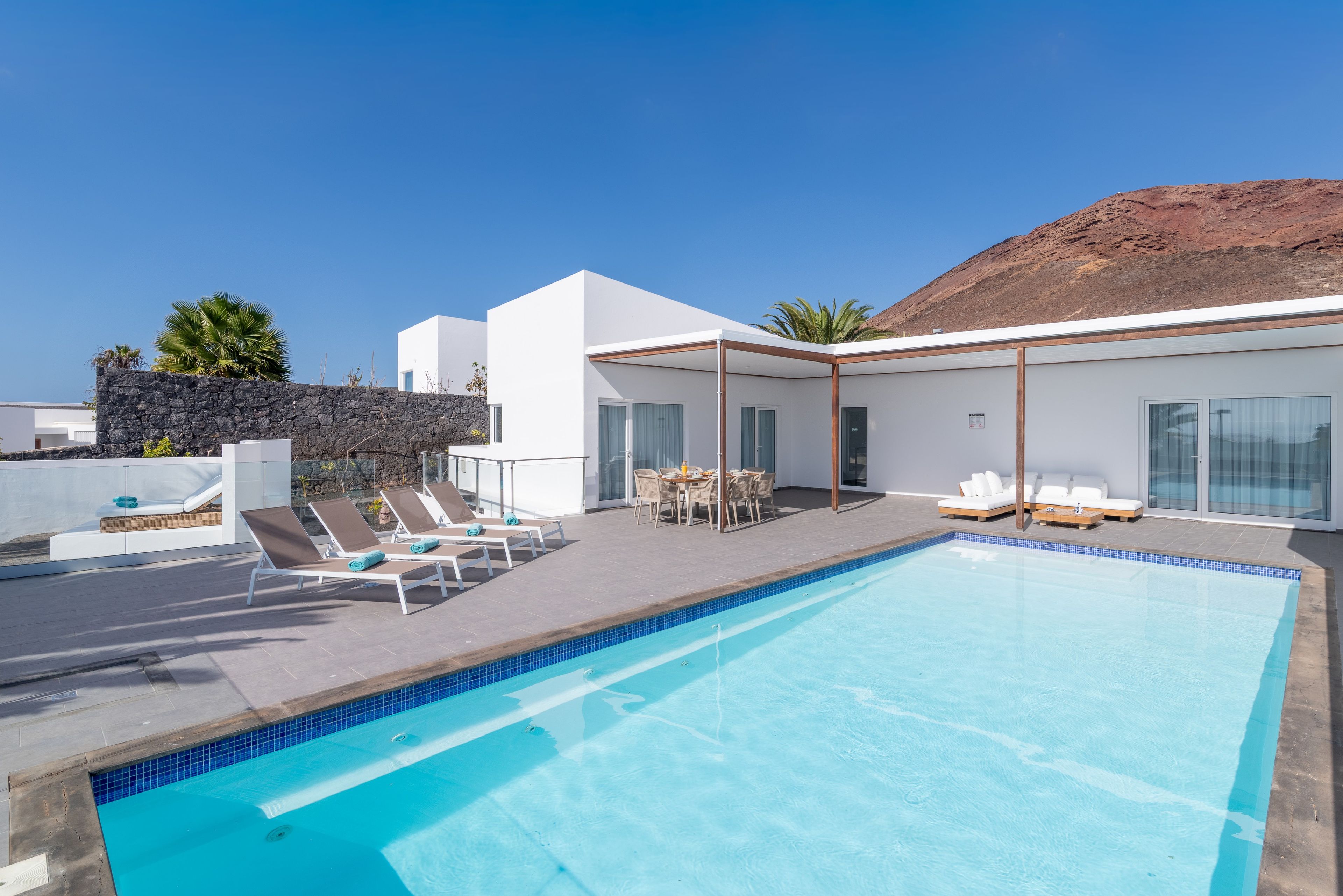 A modern poolside area with a clear blue pool, lounge chairs, and a dining set.