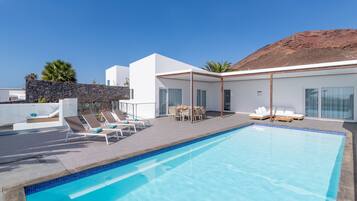 A modern poolside area with a clear blue pool, lounge chairs, and a dining set.