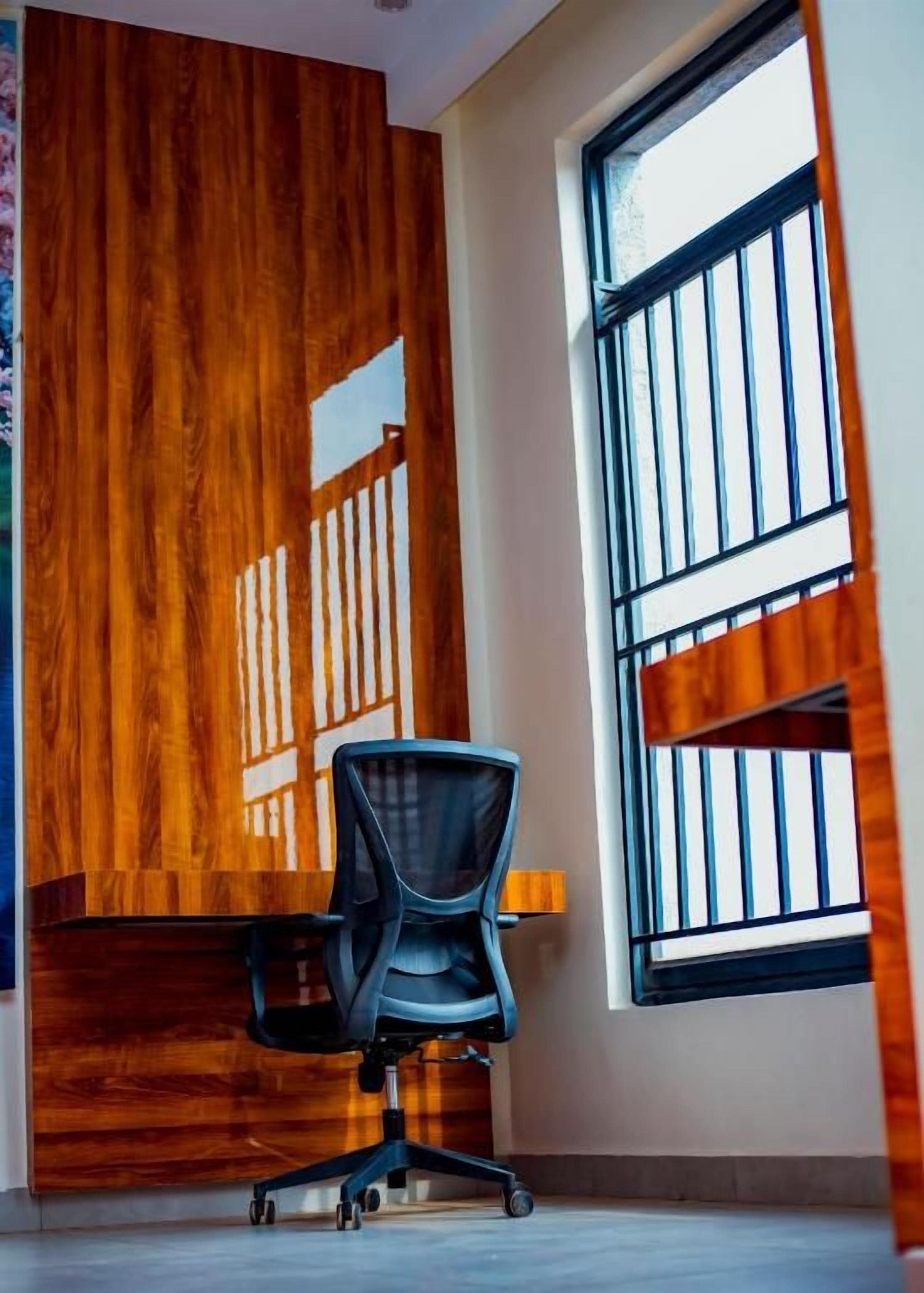 A room with a wooden accent wall, a window with bars, and a black office chair.