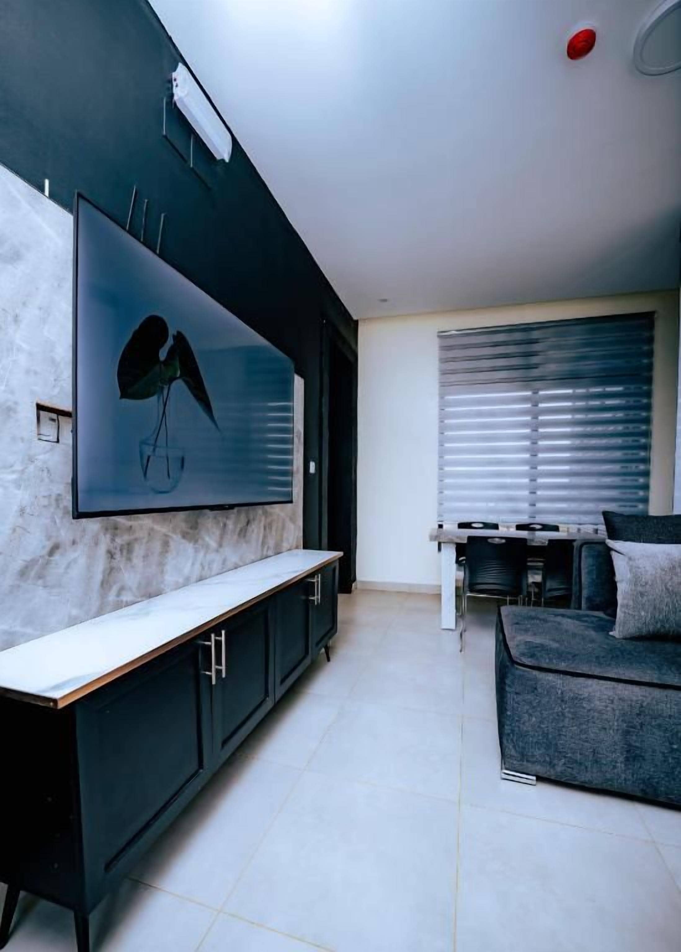 A modern living space with a large flat-screen TV mounted on a wall, a dark-colored sofa, and a kitchen area with a stove.