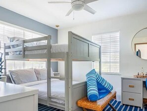A bunk bed room with a ceiling fan, a bedside table, a chair with a cushion, and a small desk with drawers. - Paradise Calling Florida (Monroe County)