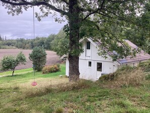 Ein weißes, zweistöckiges Haus mit geneigtem Dach, umgeben von Bäumen und einer Wiese.