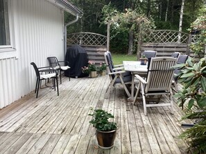 Eine Holzterrasse mit Tisch und Stühlen, umgeben von Kübelpflanzen und einem Holzzaun.