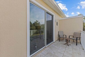 A balcony with a sliding glass door, a small table, and two chairs. - Serenity Resort | Private Pool Townhome | 3Bd3bath (Four Corners)