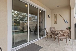 Eine überdachte Terrasse mit Glastür zum Poolbereich, einem Tisch mit Stühlen und einem 'WELCOME'-Schild an der Wand.