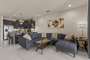 A modern living room with a grey sectional sofa, a coffee table, and a kitchen in the background. - Serenity Resort | Private Pool Townhome | 3Bd3bath (Four Corners)
