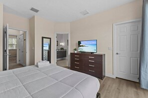 A bedroom with a bed, a dresser, a television, and a bathroom visible through an open door. - Serenity Resort | Private Pool Townhome | 3Bd3bath (Four Corners)