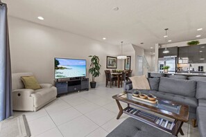 A modern living room with a flat-screen TV, a sofa, a coffee table, and a dining area with chairs and a plant. - Serenity Resort | Private Pool Townhome | 3Bd3bath (Four Corners)