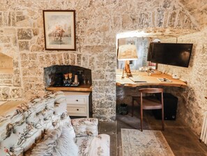 A stone-walled room with a wooden desk, a television, a sofa, and a framed picture on the wall. - The Bakery Hotel Room (Barry)