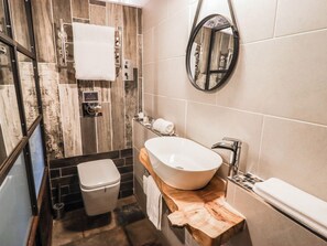 A modern bathroom with a wooden vanity, a freestanding toilet, a large mirror, and a towel rack. - The Bakery Hotel Room (Barry)