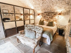 A room with a stone wall, a bed with pillows, a sofa with a throw, and a wooden cabinet. - The Bakery Hotel Room (Barry)