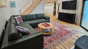 Ein modernes Wohnzimmer mit einer Eckcouch, einem runden Couchtisch, einem Fernseher und einer Treppe mit Holzbalkon.