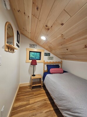 A bedroom with a wooden ceiling, a bed with blue and red bedding, a small bedside table with a lamp, and a wall-mounted TV. - Camp Jay Cloud - Views of the slopes! 4 bedroom 2 bath 
VAST trails! (Jay)