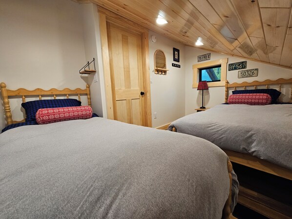 A room with two beds, wooden headboards, a wooden door, and wall-mounted signs indicating Vermont locations.