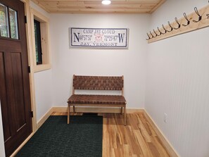 Una habitación con un banco de madera, un cartel con coordenadas y un perchero.