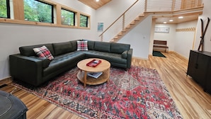 Ein modernes Wohnzimmer mit einer Eckcouch, einem Couchtisch, einem gemusterten Teppich und einer Treppe, die zu einer oberen Etage führt.