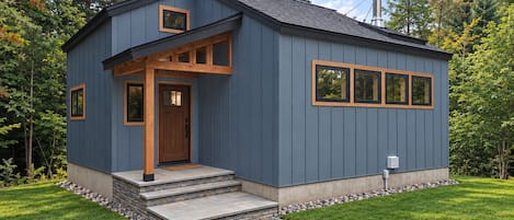 A modern house with a grey exterior, a wooden front door, and a chimney.