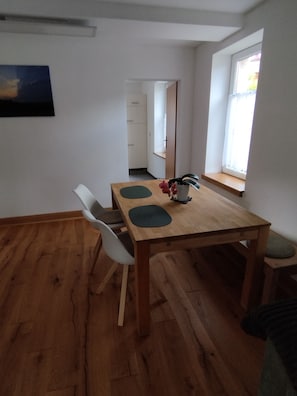 Un coin repas avec une table en bois, deux chaises, un vase de fleurs et une fenêtre donnant sur un beau paysage.