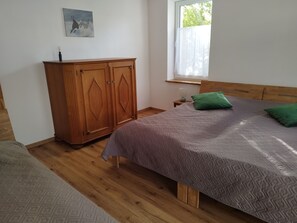 A bedroom with a bed, wooden wardrobe, and a window with a view of greenery.