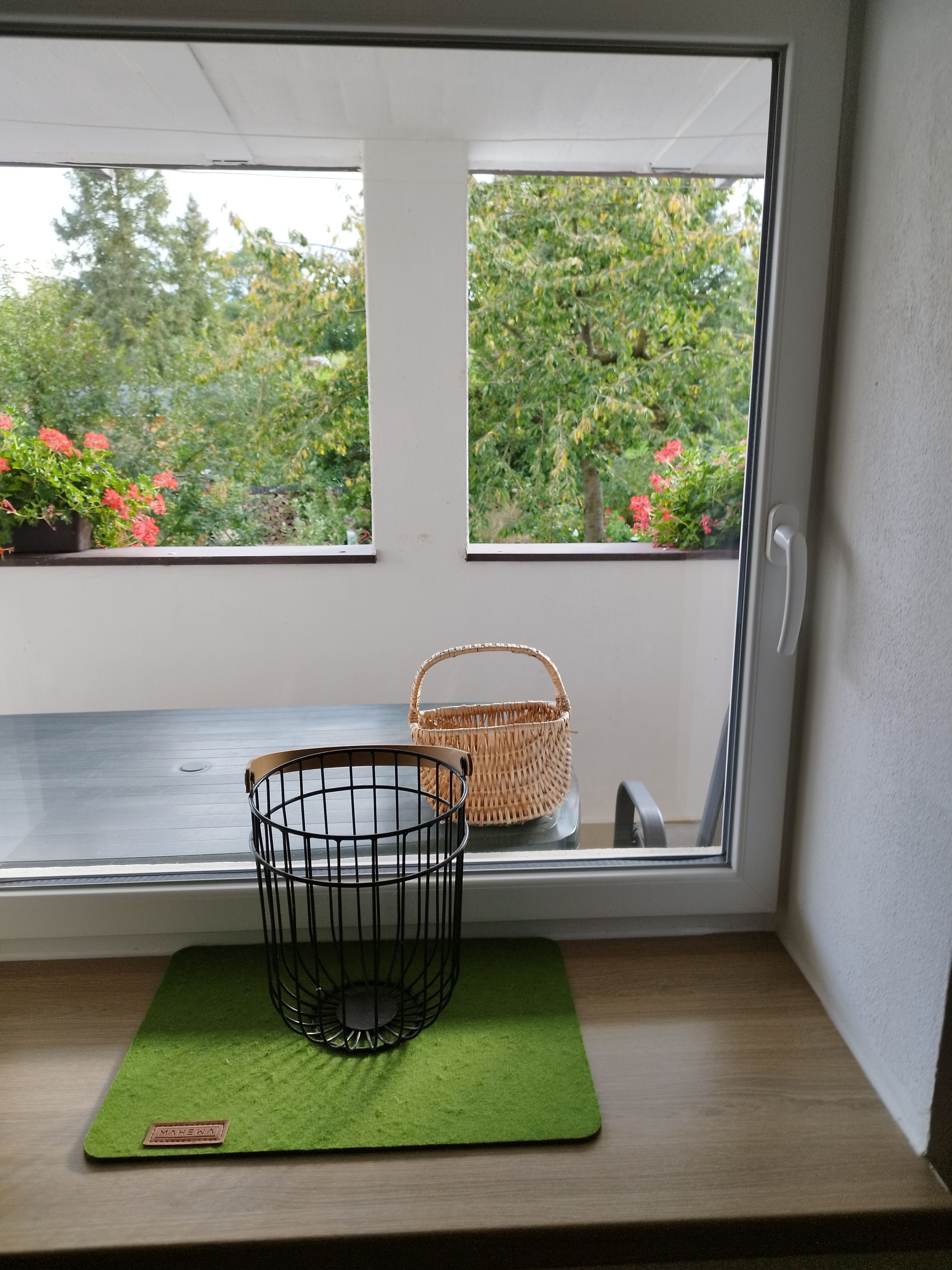 Ein Fenster mit Blick auf Grün und ein Korbwäschekorb auf einem Regal.