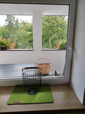 Une fenêtre donnant sur un paysage verdoyant et un panier en osier posé sur une étagère.