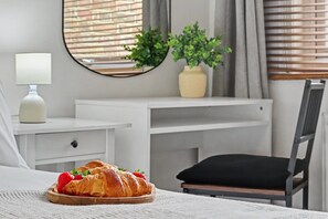 Quarto com cama, mesa de cabeceira com abajur, escrivaninha com planta e uma cadeira.